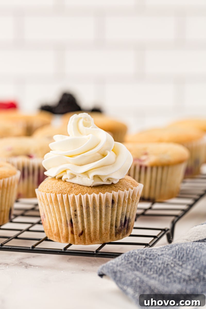A freshly frosted berry cupcake sitting on a wire rack, surrounded by other unfrosted cupcakes, waiting to be adorned with creamy goodness.