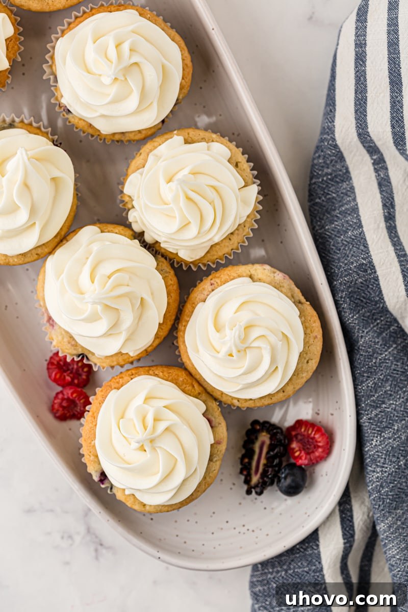 An overhead view of a dozen freshly baked berry cupcakes arranged neatly on a pristine white serving tray, showcasing their golden-brown tops and vibrant berry peeks.