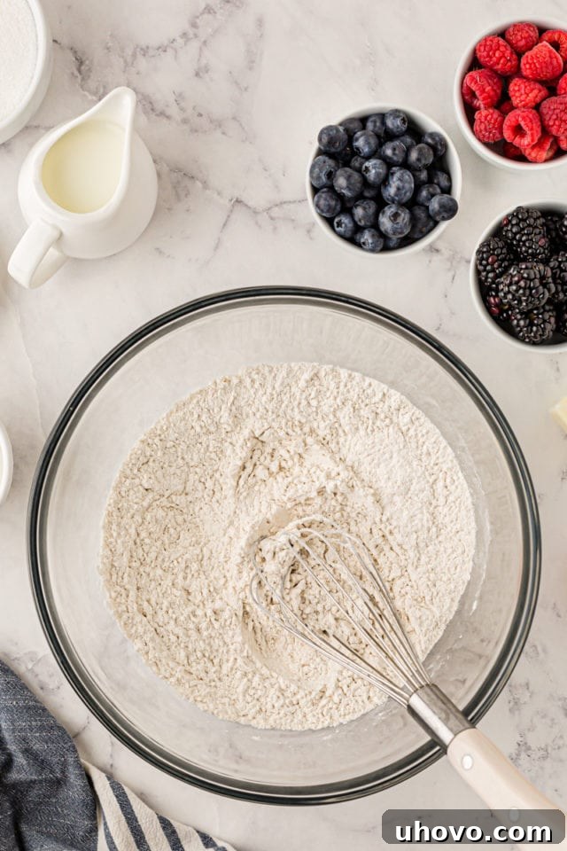 An overhead shot showing the dry ingredients for the berry cupcakes (flour, baking powder, baking soda, salt) expertly whisked together in a glass mixing bowl, ensuring even distribution.