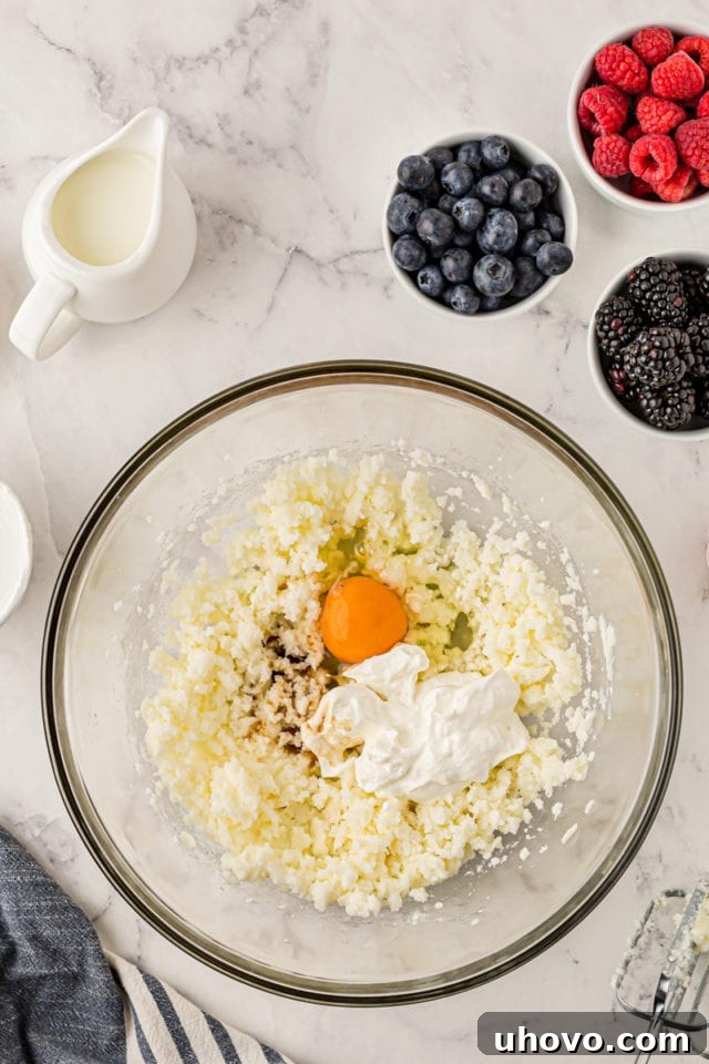 An overhead shot showing the addition of egg, vanilla extract, and sour cream into the creamed butter and sugar mixture in a glass bowl, ready for further mixing.