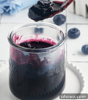 A spoonful of homemade blueberry compote held over a jar of compote, highlighting its vibrant color and texture.