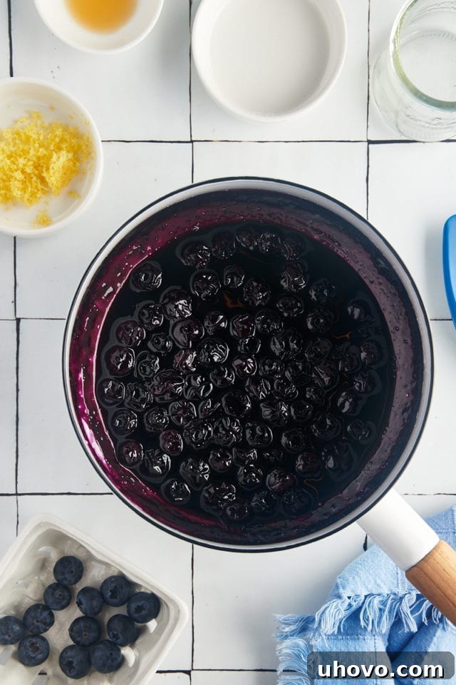 An overhead view of the blueberry compote gently simmering in a saucepan, with berries starting to break down and release their juices.