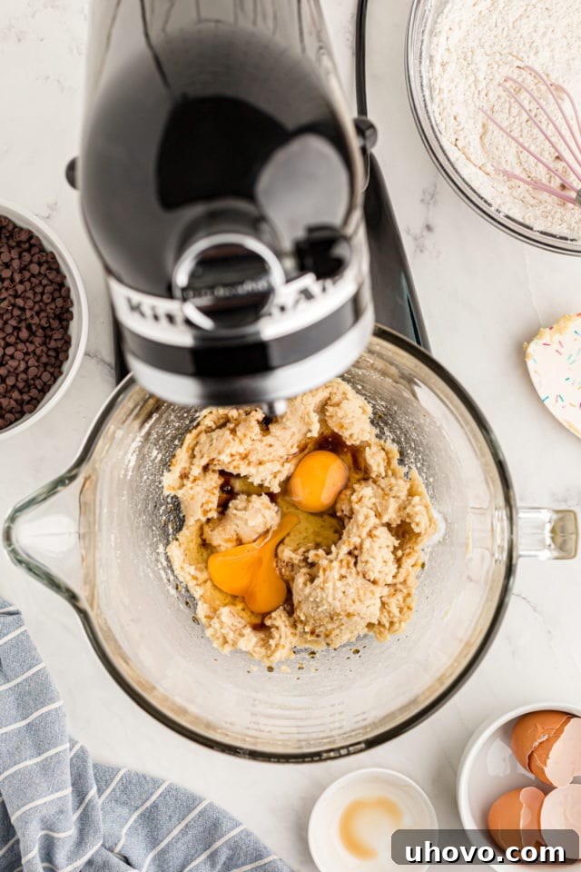 overhead view of eggs and vanilla added to cookie dough in the bowl of a stand mixer