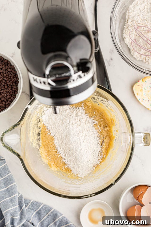 overhead view of flour added to cookie dough in the bowl of a stand mixer