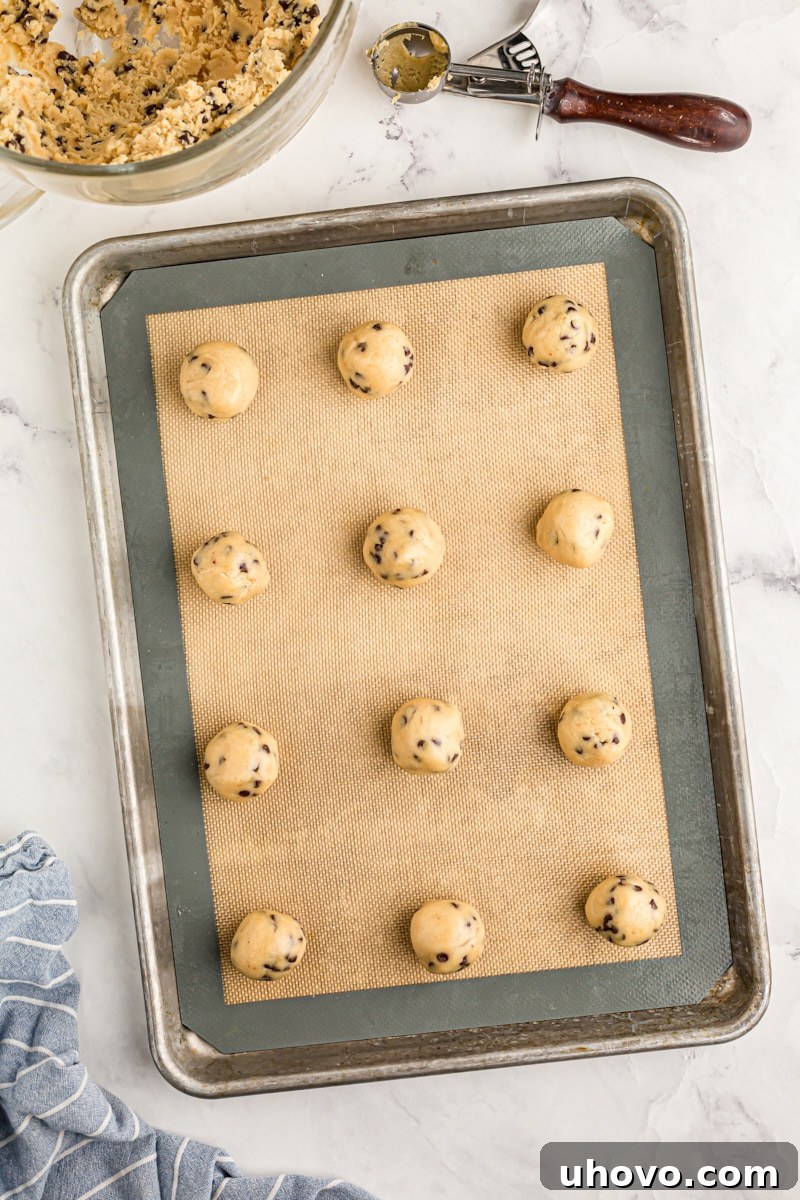 overhead view of portioned chocolate chip cookie dough on a baking sheet lined with a silicone liner