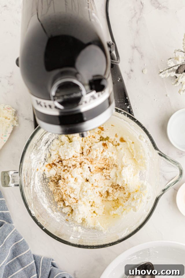 overhead view of vanilla and hot water added to frosting mixture in the bowl of a stand mixer