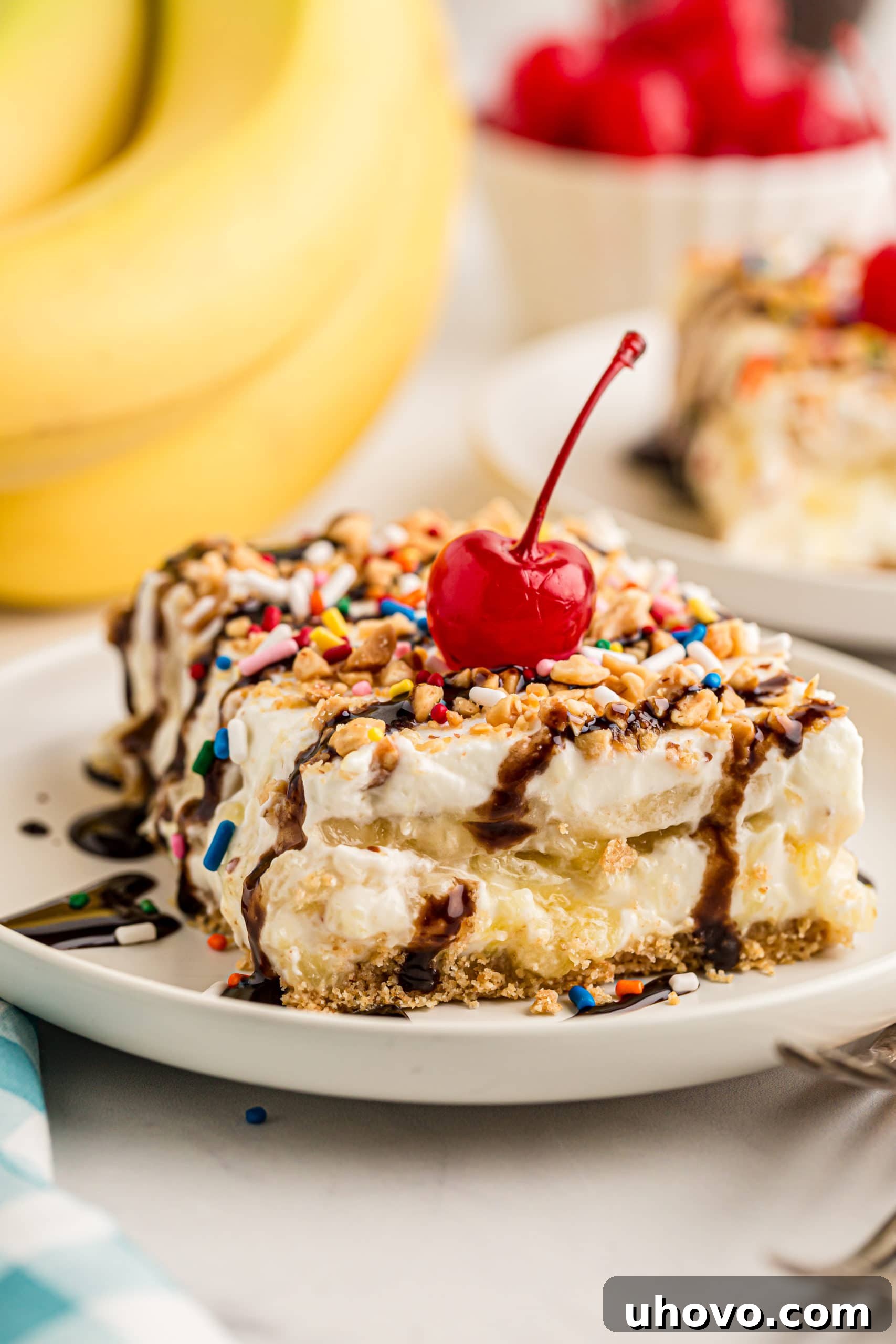 Slice of banana split cake topped with cherry and chocolate syrup, showcasing its creamy layers and delicious toppings.