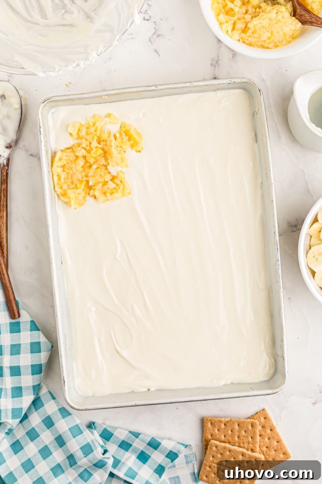 Crushed pineapple being spread evenly over the cream cheese filling layer of the banana split cake.