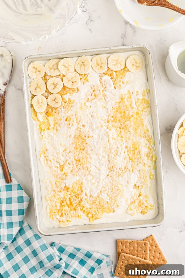 Fresh banana slices being arranged over the pineapple layer of the banana split cake.