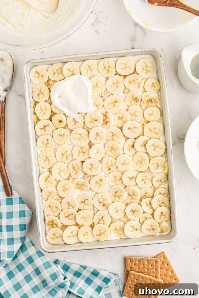 Overhead view of the fluffy whipped cream being spread over the banana and pineapple layers of the banana split cake.