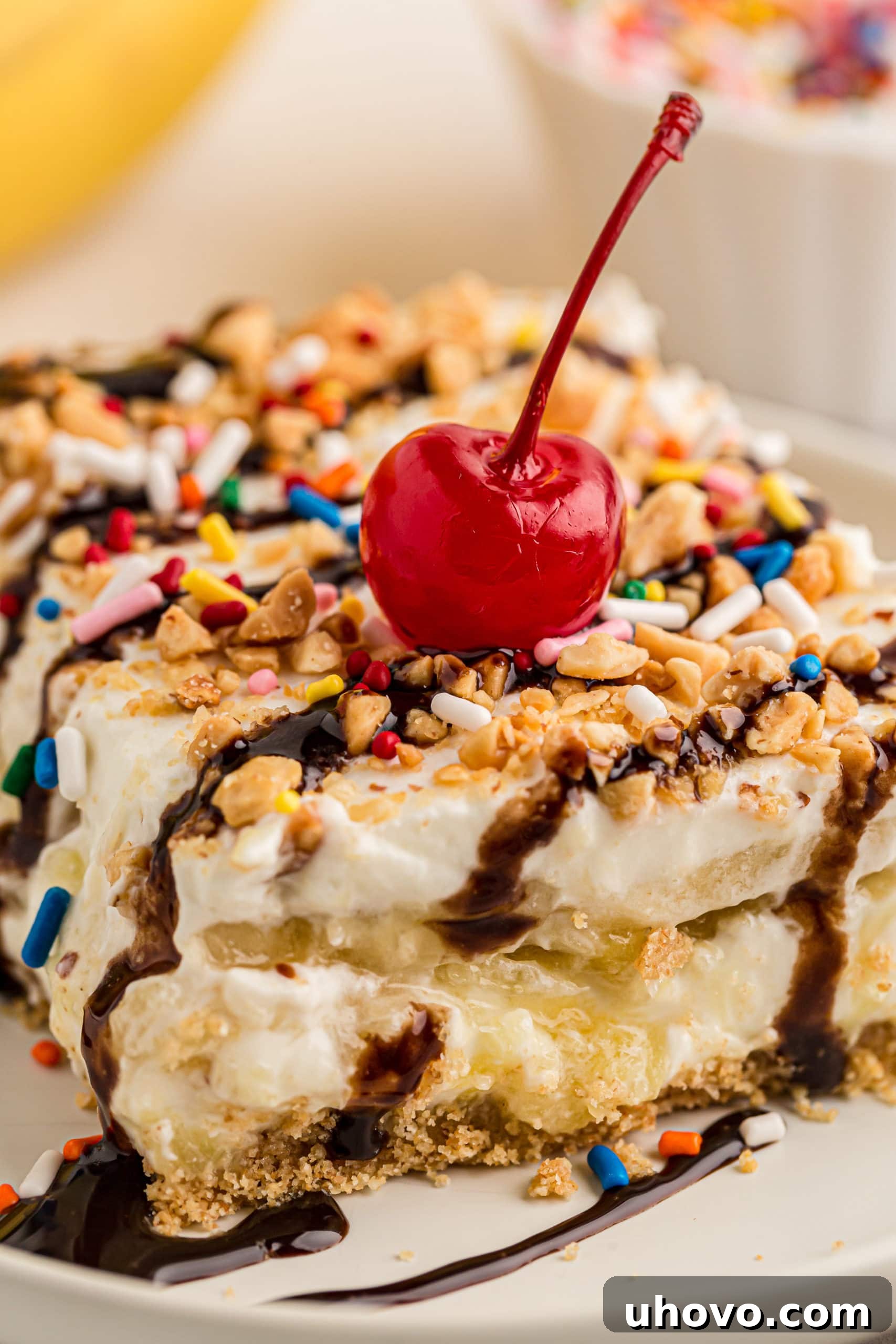Closeup of a single slice of banana split cake, artfully topped with a maraschino cherry and a drizzle of chocolate.