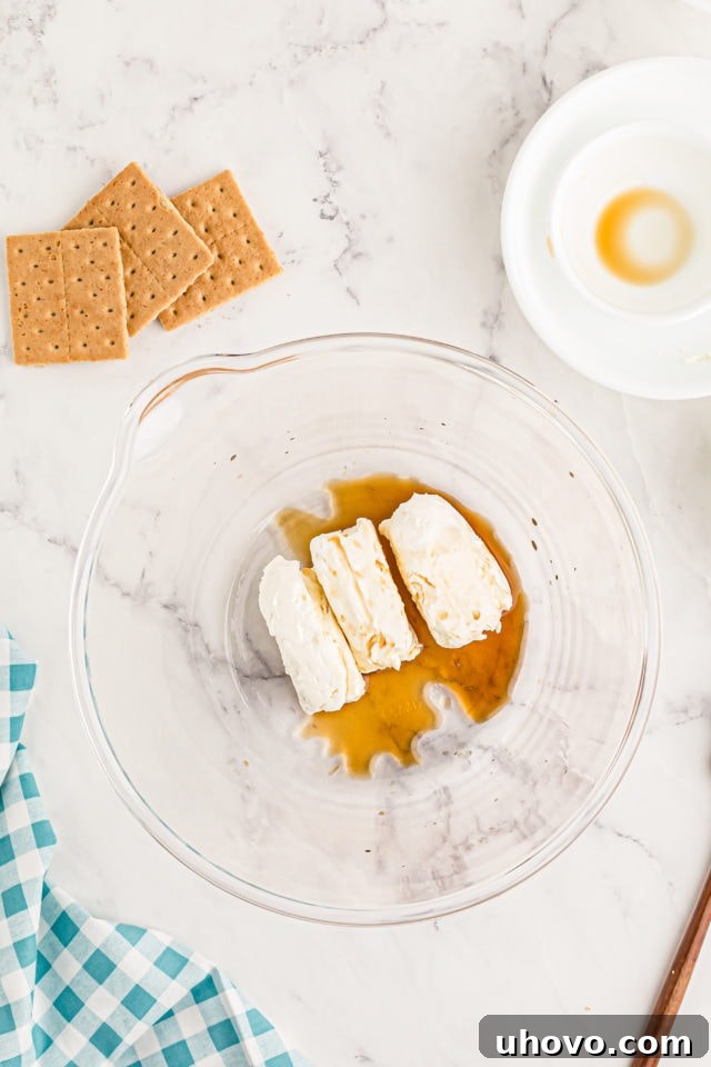 Overhead view of softened cream cheese and vanilla extract in a mixing bowl, ready to be beaten.