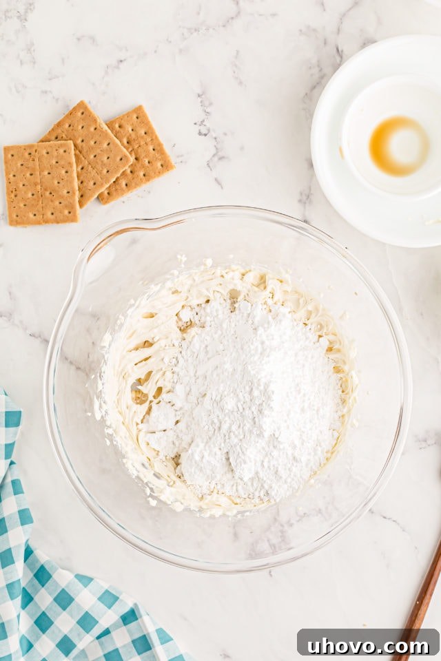 Overhead view of confectioners' sugar being added to the whipped cream cheese mixture in a bowl.