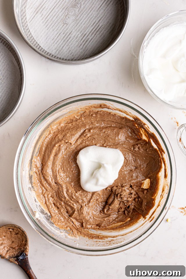 Gently folding whipped egg whites into the prepared German chocolate cake batter to lighten the texture.