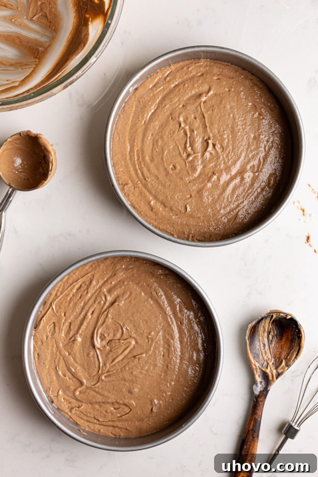 Evenly divided German chocolate cake batter in two round baking pans, ready for the oven.