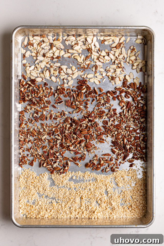 Chopped pecans, sliced almonds, and hazelnuts spread on a baking sheet, ready for toasting to enhance their flavor.