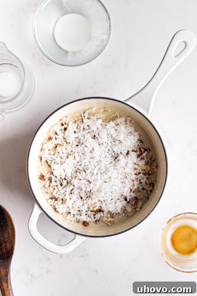 Flaked coconut and toasted nuts being stirred into the thickened German chocolate cake frosting mixture in a saucepan.