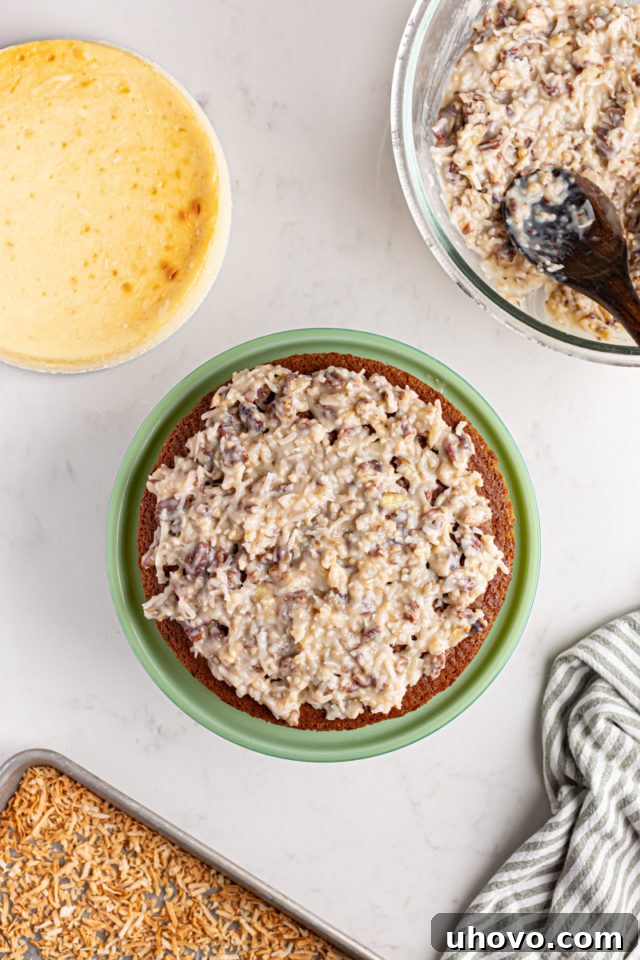Spreading a layer of creamy coconut-pecan frosting over the first chocolate cake layer on a cake plate.