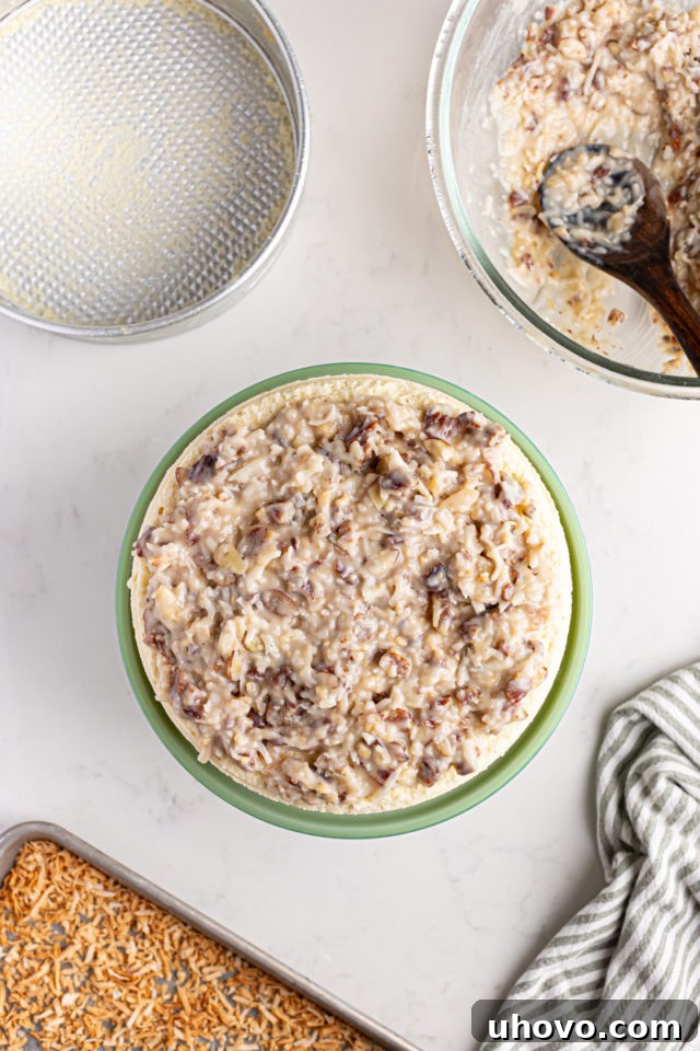 Placing the chilled cheesecake layer on top of the frosted chocolate cake, then spreading more coconut-pecan frosting over the cheesecake.