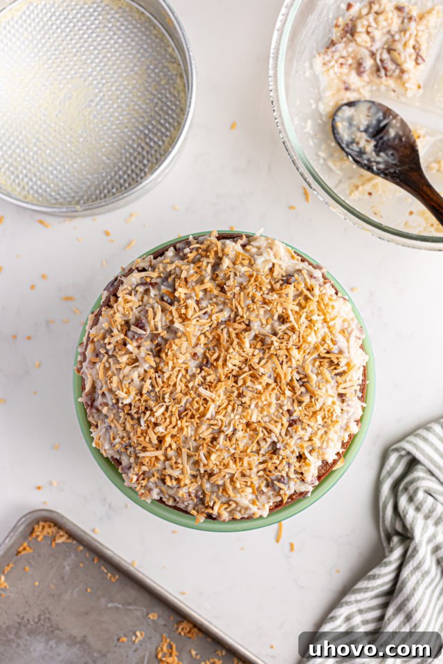 Overhead view of a beautifully layered German chocolate cheesecake, topped with the final layer of frosting and a sprinkle of toasted coconut, ready for chilling.