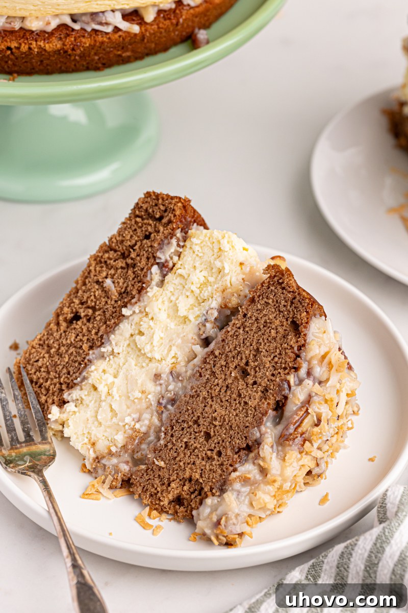 A perfectly cut slice of German chocolate cheesecake on a white plate with a fork, showing off its distinct layers of chocolate cake, creamy cheesecake, and rich coconut-pecan frosting.