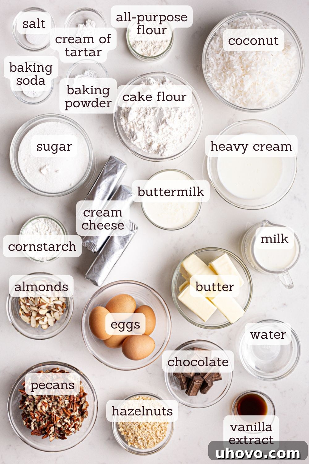 Assortment of fresh ingredients laid out, ready for baking German chocolate cheesecake, including blocks of cream cheese, butter, eggs, bags of flour, and containers of milk and cream.