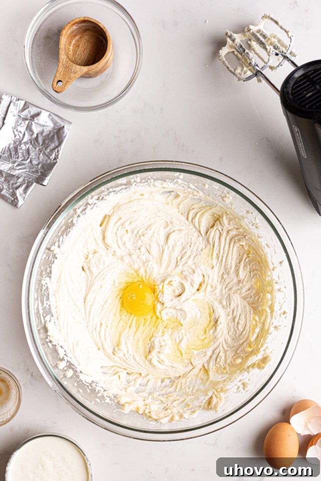 Adding eggs one by one to a creamy cheesecake batter in a mixing bowl, ensuring smooth incorporation.