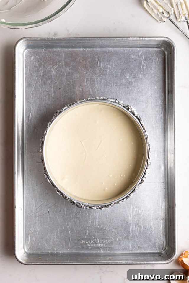Cheesecake batter poured into a foil-wrapped springform pan, placed inside a larger shallow pan for a water bath, ready for baking.