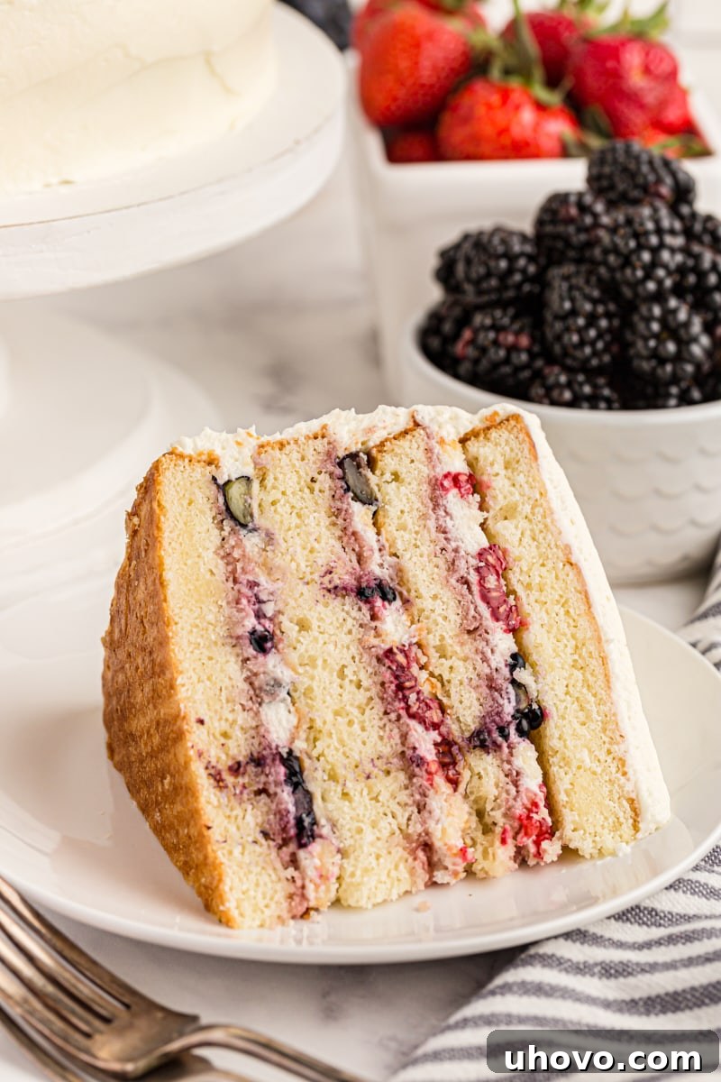 Slice of chantilly cake on its side on a white cake, with bowls of berries in background