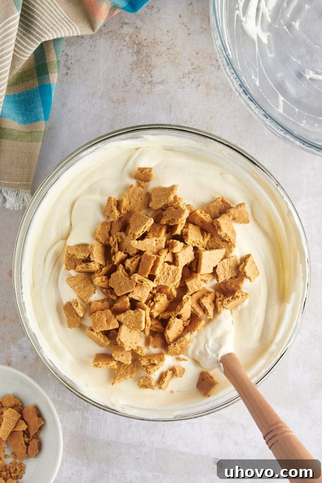 Overhead view of graham cracker pieces added to mixing bowl of ice cream mixture