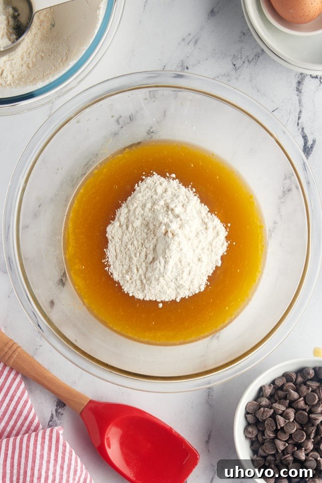An overhead shot depicting the dry flour mixture being carefully added to the vibrant wet ingredients in a glass mixing bowl, initiating the final dough preparation.