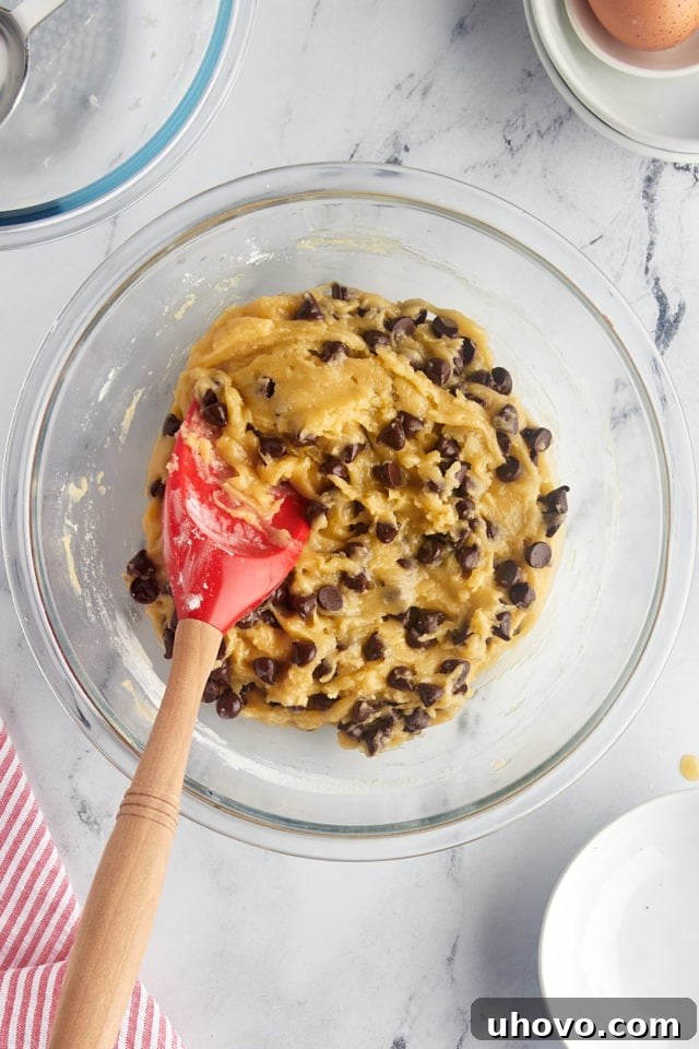 An overhead view of the completed chocolate chip cookie cake dough, perfectly mixed and filled with chocolate chips, resting in a glass mixing bowl, ready for baking.