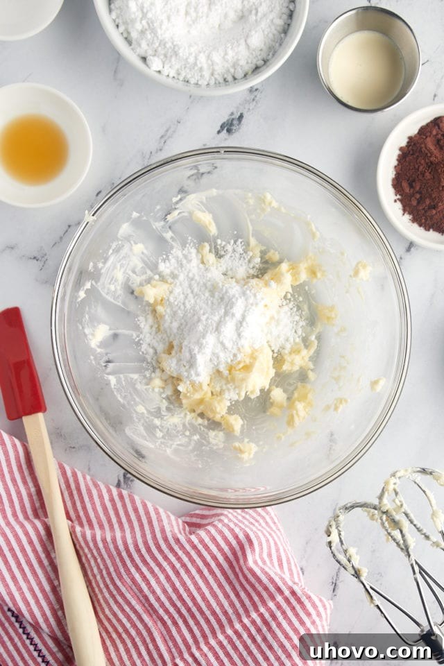 An overhead shot showing the initial stages of frosting preparation, with creamed butter and confectioners' sugar beautifully blended in a glass mixing bowl.