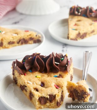 A slice of chocolate chip cookie cake on a white plate with more servings in the background