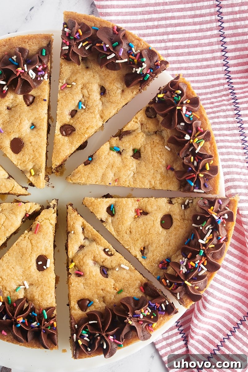 An overhead view of a perfectly sliced chocolate chip cookie cake resting on a white cake stand, showcasing its soft interior and abundant chocolate chips.