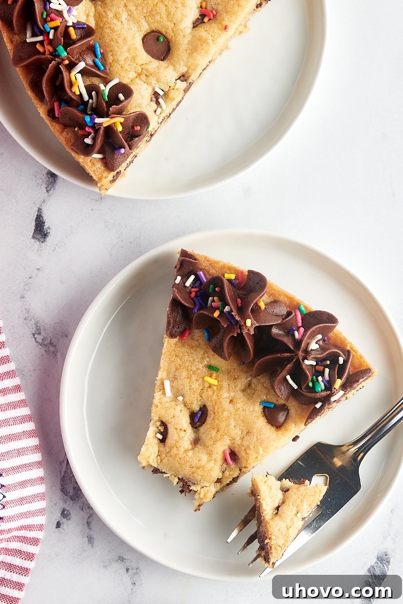 An overhead view of a delicious slice of chocolate chip cookie cake on a white plate, with a fork holding a bite-sized piece, highlighting the cake's soft texture and melted chocolate.