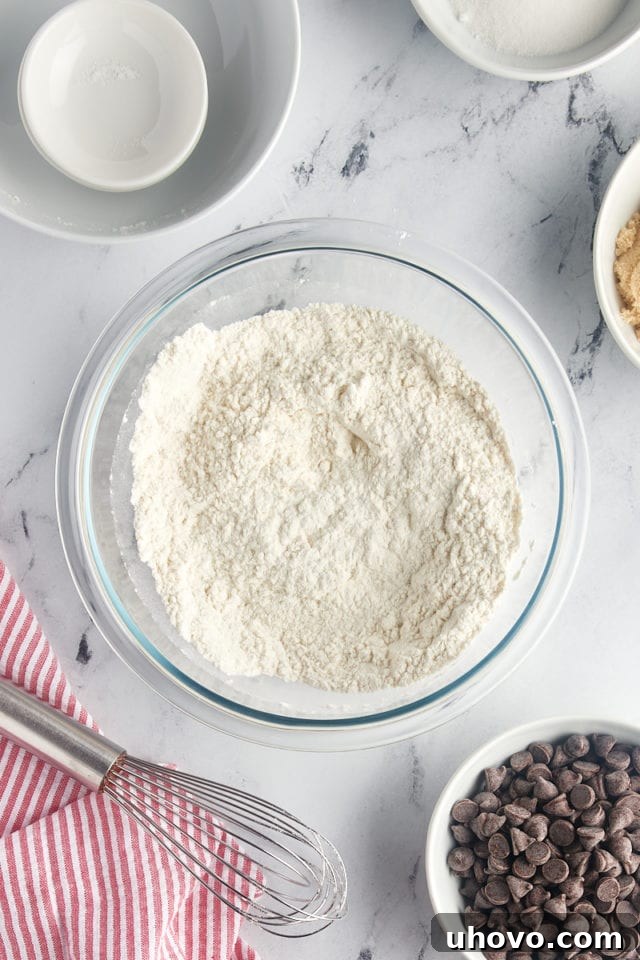 A close-up, overhead shot of the dry ingredients for the chocolate chip cookie cake, now expertly whisked together in a glass mixing bowl, creating a uniform mixture.