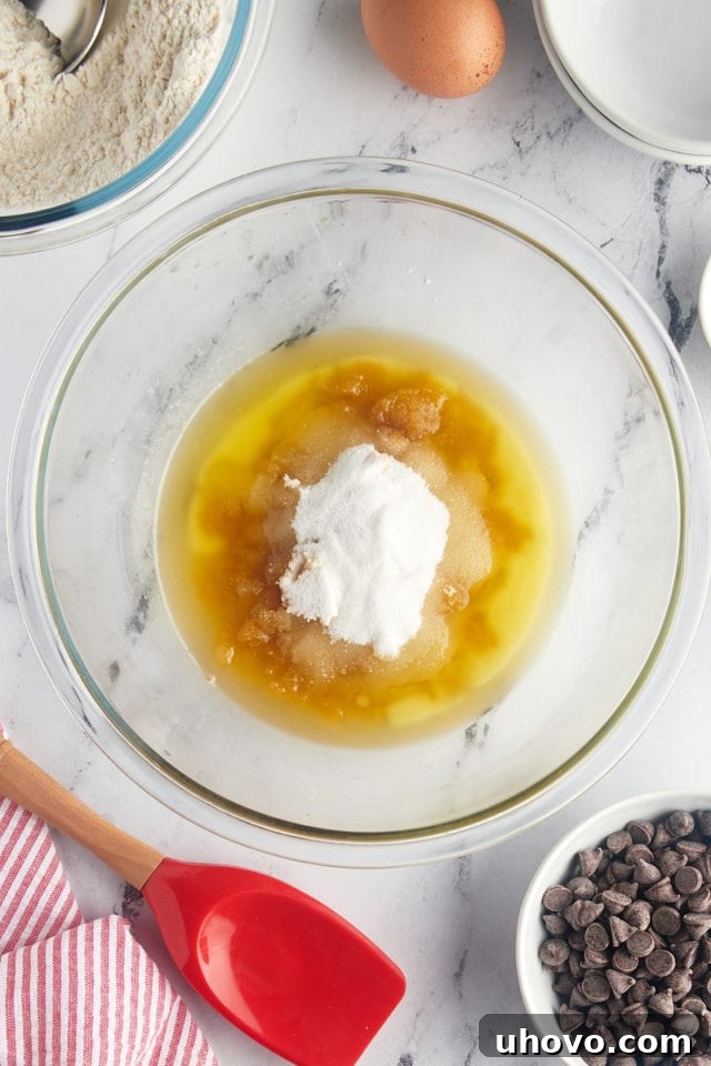 An overhead shot of melted butter, light brown sugar, and granulated sugar perfectly combined in a clear glass mixing bowl, forming a rich, cohesive mixture.
