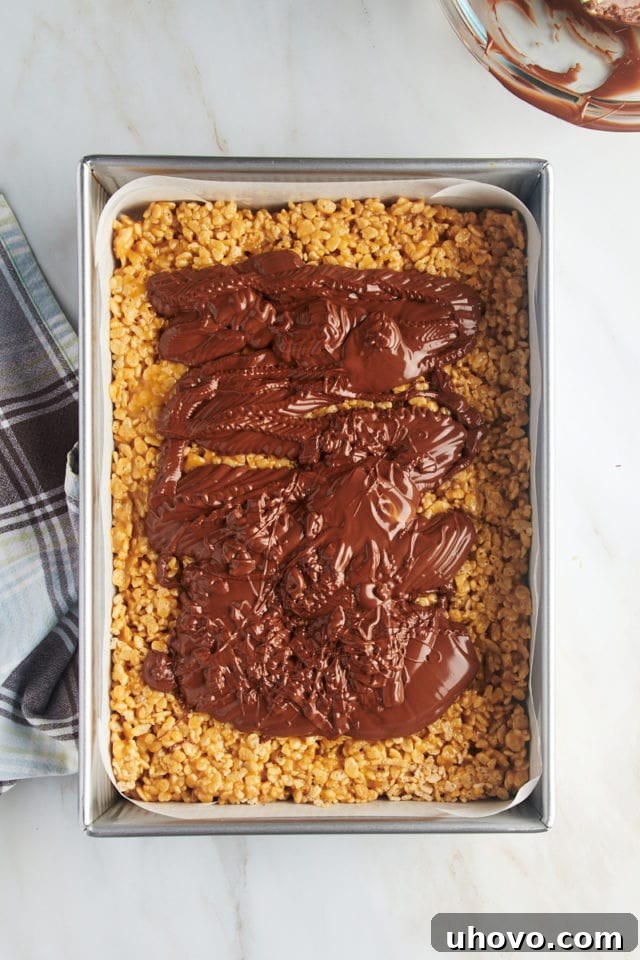 Overhead view of melted chocolate and butterscotch added to rice crispy layer in pan.