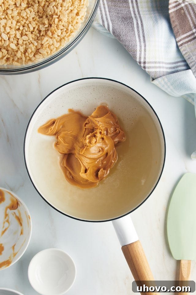 Overhead view of peanut butter added to syrup in saucepan, being stirred in.