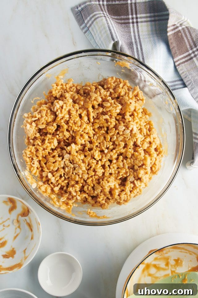 Overhead view of peanut butter and crispy rice mixture in glass bowl, evenly coated.