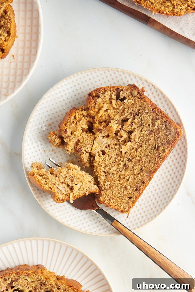 Overhead view of peanut butter banana bread slice on white plate with fork, highlighting its moist texture and inviting aroma.