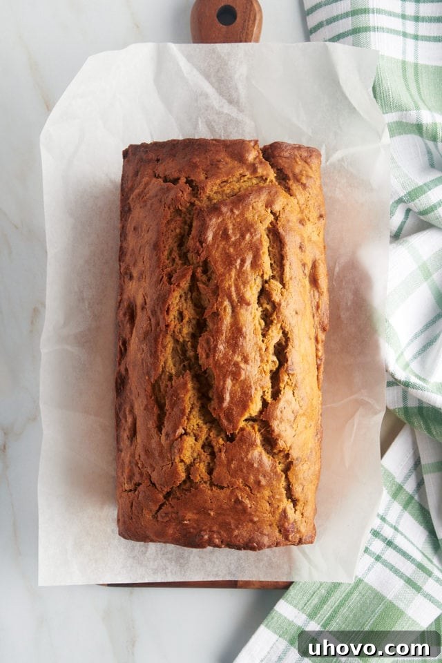 Overhead view of a perfect, whole loaf of peanut butter banana bread resting on a rustic wooden cutting board, cooling.