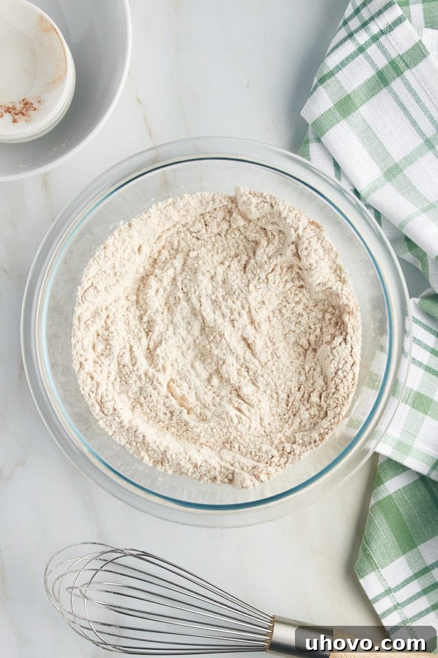 Overhead view of dry ingredients, flour, cinnamon, baking powder, baking soda, and salt, perfectly combined in a glass mixing bowl.