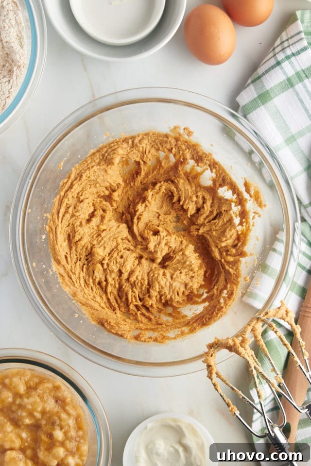 Overhead view of wet ingredients, including butter, brown sugar, and peanut butter, being creamed together in a mixing bowl until light and fluffy.