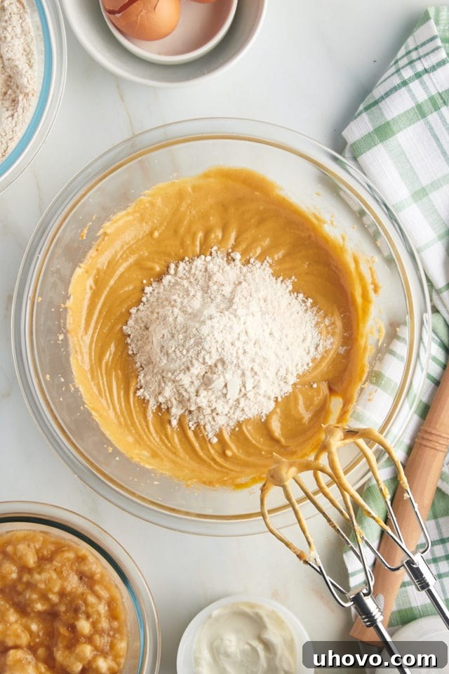 Overhead view of the dry flour mixture being gradually added to the wet batter in a mixing bowl, combining slowly.