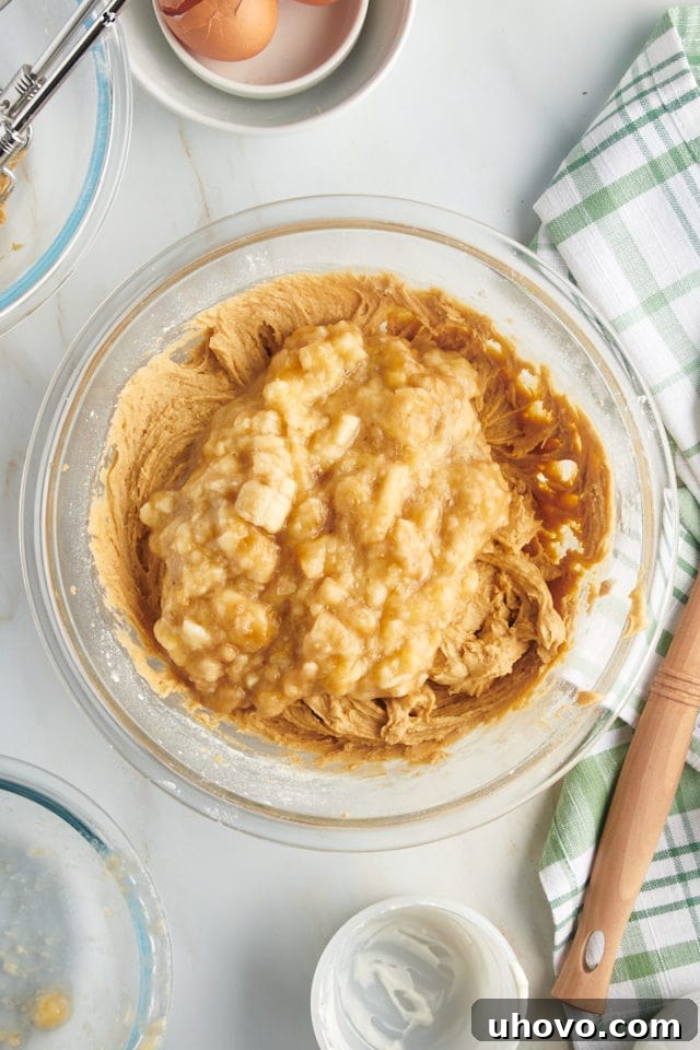 Overhead view of the mashed ripe bananas being gently added to the mixing bowl, ready to be folded into the bread batter.