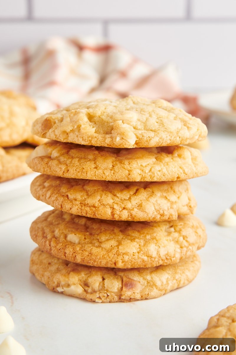 A neatly stacked tower of five freshly baked white chocolate macadamia nut cookies, highlighting their golden-brown edges and visible white chocolate chunks and macadamia nut pieces.