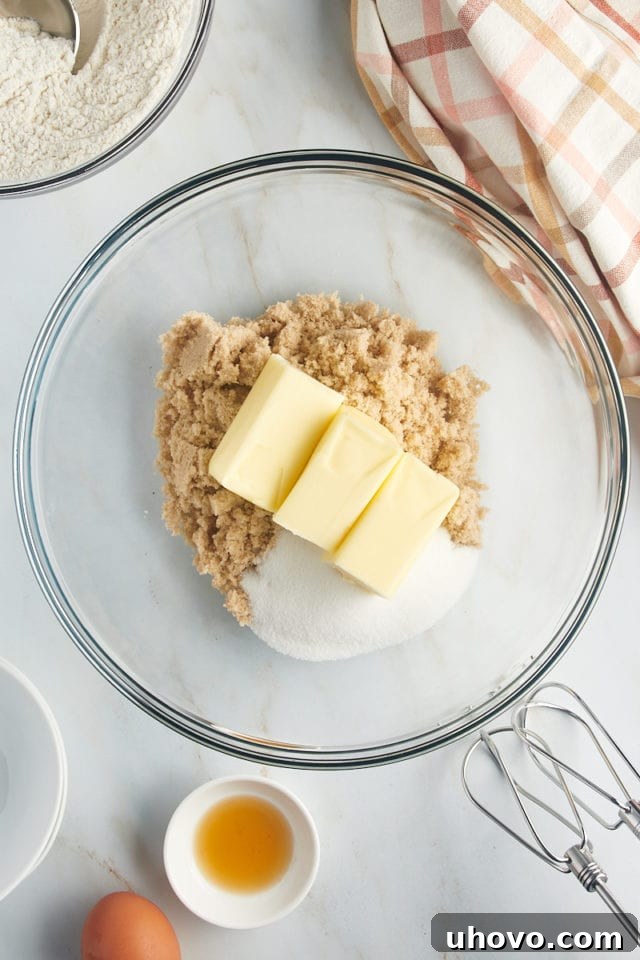 Overhead view of softened butter and two types of sugar (light brown and granulated) in a mixing bowl, ready to be creamed together.