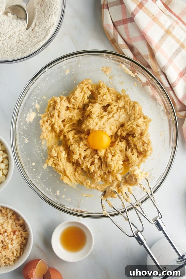 Overhead view showing a single egg yolk being added to the creamed butter and sugar mixture in a mixing bowl, enhancing the richness of the cookie dough.